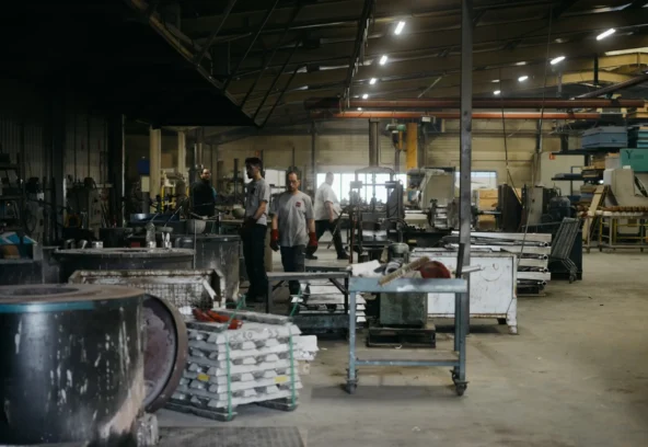 Vue d'ensemble de l'atelier avec opérateurs, lingots empilés et postes de moulage