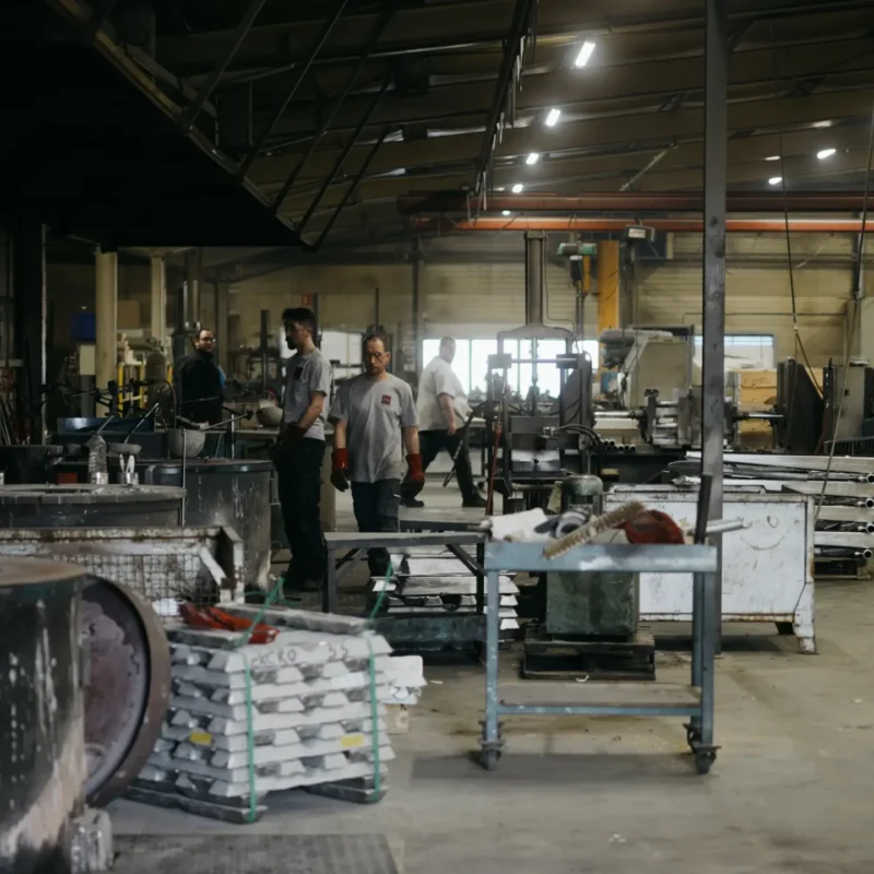 Vue d'ensemble de l'atelier avec opérateurs, lingots empilés et postes de moulage
