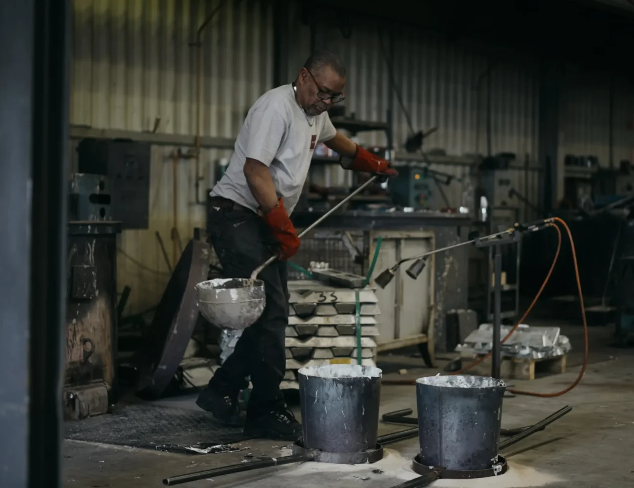 Opérateur coulant l'aluminium dans un moule, dans une vue large de l'atelier de fonderie