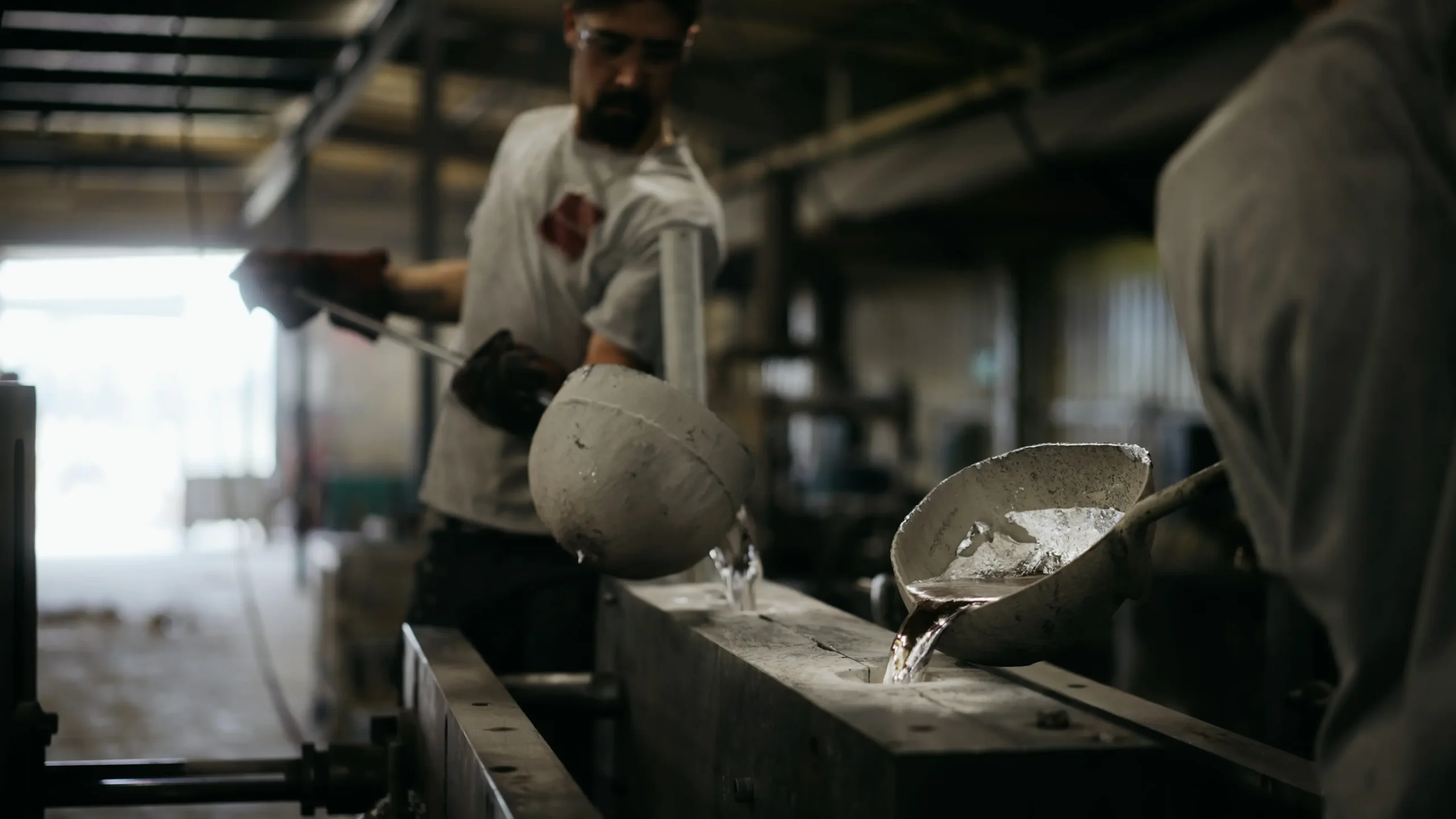 Fondeur versant l'aluminium liquide d'une louche dans un moule en sable de fonderie